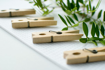 Eco friendly household items. Wooden clothes pins lay on white towel at the table with green plant branches, grey background.