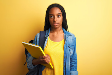 African american student woman wearing backpack and book over isolated yellow background with a confident expression on smart face thinking serious