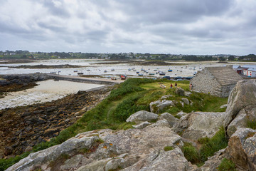 Coastal region of Brittany with houses, grass and rocks, low tide with small boats on the sand
