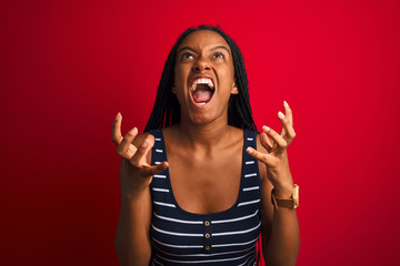 Young african american woman wearing striped t-shirt standing over isolated red background crazy...