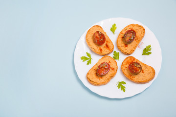 Tostadas con hummus y tomates cherry en un plato con perejil sobre fondo azul celeste.