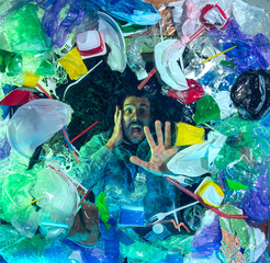 Man drowning in water under plastic recipients pile, garbage. Used bottles and packs filling world...