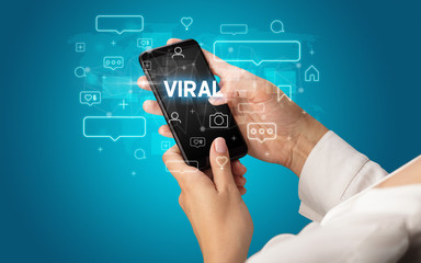 Female hand typing on smartphone with VIRAL inscription, social media concept
