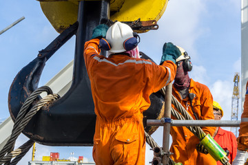Offshore workers installing a heavy lifting sling onto a crane hook on board a construction work...