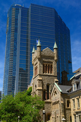 Fototapeta na wymiar Old St Andrews presbyterian church tower against modern blue glass highrise office tower Toronto