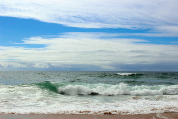 Fototapeta premium Atlantic ocean, green water, waves, ocean foam, wet sand, white clouds, blue bright saturated sky, Portugal