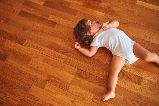 Beautiful toddler child girl wearing white bodysuit lying down on the floor using pacifier