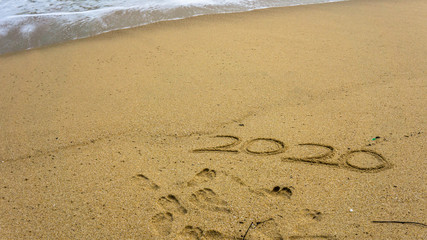 Numbers 2020 year on the sea shore, message handwritten in the golden sand on beautiful beach background.