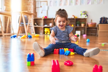 Beautiful toddler sitting on the floor playing with building blocks toys at kindergarten