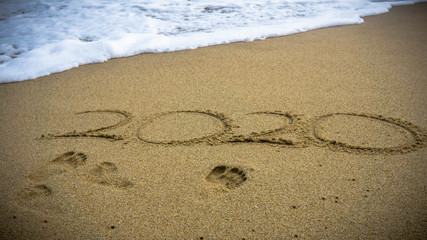 Numbers 2020 year on the sea shore, message handwritten in the golden sand on beautiful beach background.