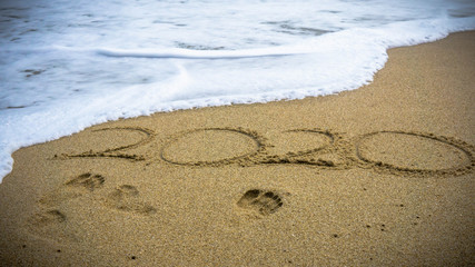 Numbers 2020 year on the sea shore, message handwritten in the golden sand on beautiful beach background.