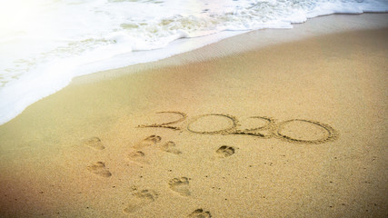 Numbers 2020 year on the sea shore, message handwritten in the golden sand on beautiful beach background.