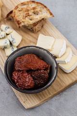 Top view of a cheese board with Brie, blue cheese, toasted bread and focus on sun-dried tomatoes with.