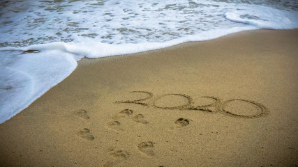 Numbers 2020 year on the sea shore, message handwritten in the golden sand on beautiful beach background.