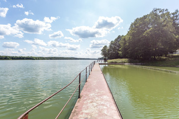 pier on the shore of a large lake in summer day with beautiful clouds.  sky reflection