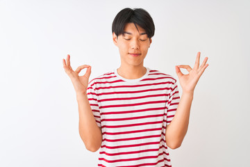 Young chinese man wearing casual striped t-shirt standing over isolated white background relax and smiling with eyes closed doing meditation gesture with fingers. Yoga concept.