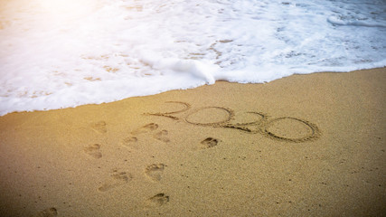 Numbers 2020 year on the sea shore, message handwritten in the golden sand on beautiful beach background.