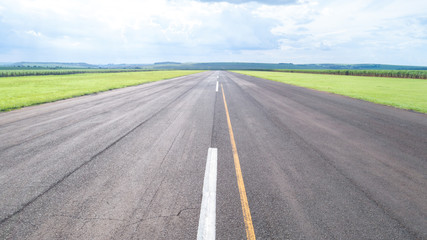 Aerial view of paved airplane runway on Brazil. Small propeller airplanes remote airstrip with Sugar Cane plantation in background. - obrazy, fototapety, plakaty