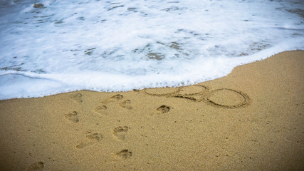 Numbers 2020 disappear on the sea shore, message handwritten in the golden sand on beautiful beach background.