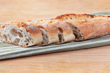 Slices of freshly baked French baguette on an olive striped cotton fabric as a catering concept. Feature crispy crusts and airy centers. Wooden background