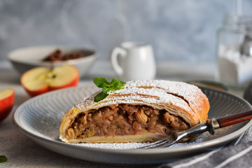 Strudel with apples, nuts and raisins on a concrete background.