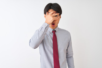 Chinese businessman wearing elegant tie standing over isolated white background peeking in shock covering face and eyes with hand, looking through fingers with embarrassed expression.