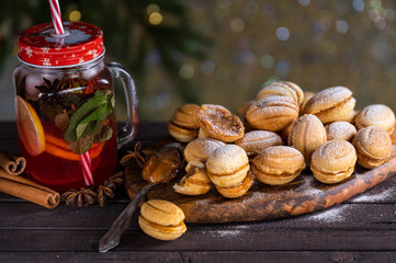 cookies with caramel milk in the form of nuts on a wooden tray with a fruit drink with spices (cinnamon and star anise) against the background of New Year's lights and a Christmas tree