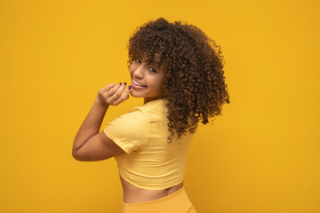 Backwards American African woman with her curly hair on yellow background. Laughing curly woman in...