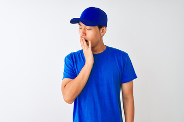 Chinese deliveryman wearing blue t-shirt and cap standing over isolated white background bored yawning tired covering mouth with hand. Restless and sleepiness.
