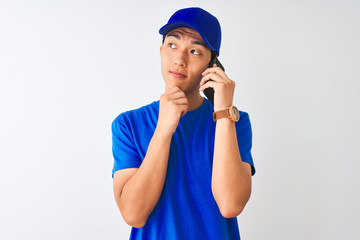 Chinese deliveryman wearing cap talking on the smartphone over isolated white background serious face thinking about question, very confused idea