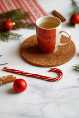 Christmas background, on the stand a red Cup of tea. Christmas decorations, holiday decorations, fir branches, red balls, cinnamon and red Lollipop cane on a light stone background top view.