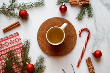 Christmas background, on the stand a red Cup of tea. Christmas decorations, holiday decorations, fir branches, red balls, cinnamon and red Lollipop cane on a light stone background top view.