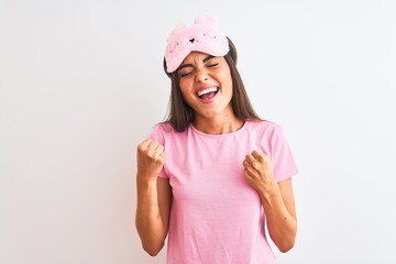 Obraz na płótnie Canvas Young beautiful woman wearing sleep mask standing over isolated white background very happy and excited doing winner gesture with arms raised, smiling and screaming for success. Celebration concept.