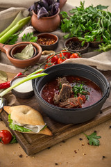 Red beetroot soup borshch with beef, wheat bun and sour cream on wooden table
