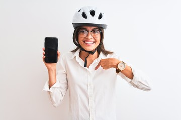 Young businesswoman wearing bike helmet holding smartphone over isolated white background with surprise face pointing finger to himself