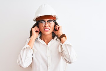 Young beautiful architect woman wearing helmet and glasses over isolated white background covering ears with fingers with annoyed expression for the noise of loud music. Deaf concept.