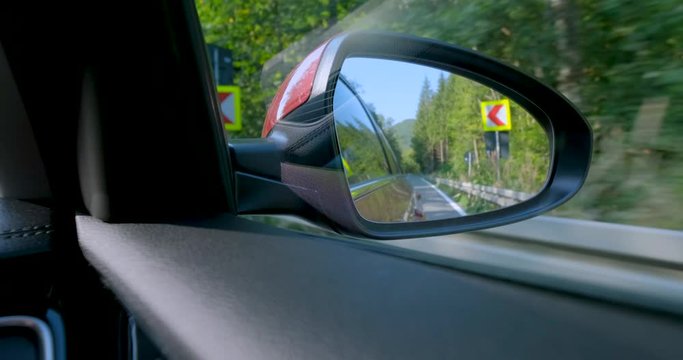 Close up of rear-view mirror of car with roa mountains and forest