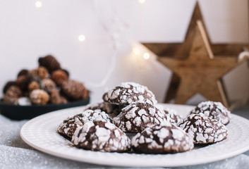 Home baked chocolate crinkle cookies in icing sugar.  Cracked chocolate biscuits in a white plate on Christmas background. Chocolate Christmas brown cookies in powdered sugar with cracks. Copy space.