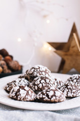Home baked chocolate crinkle cookies in icing sugar.  Cracked chocolate biscuits in a white plate on Christmas background. Chocolate Christmas brown cookies in powdered sugar with cracks. Copy space.