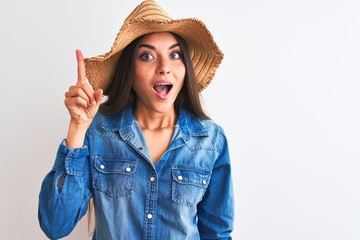 Young beautiful woman wearing denim shirt and hat standing over isolated white background pointing finger up with successful idea. Exited and happy. Number one.