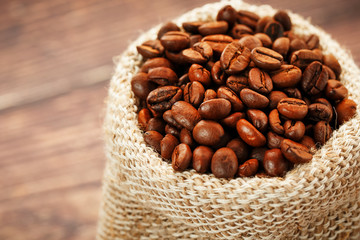 Freshly roasted aromatic coffee in a burlap bag on a wooden background.