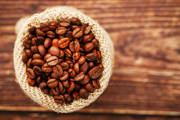 Freshly roasted aromatic coffee in a burlap bag on a wooden background.