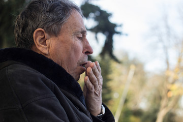 Portrait of a coughing senior man outdoors, looking down. Senior man having sickness, allergies