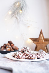 Home baked chocolate crinkle cookies in icing sugar.  Cracked chocolate biscuits in a white plate on Christmas background. Chocolate Christmas brown cookies in powdered sugar with cracks. Copy space.