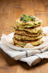 Vegetarian zucchini pancakes served with microgreens. Zucchini fritters close-up on a wooden background, front view. Delicious vegetarian food. Vegetable pancakes.