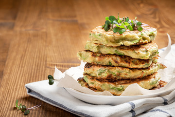 Vegetarian zucchini pancakes served with microgreens. Zucchini fritters close-up on a wooden background, front view. Delicious vegetarian food. Vegetable pancakes.