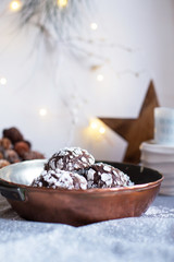 Home baked chocolate crinkle cookies in icing sugar.  Cracked chocolate biscuits in a copper pan on Christmas background. Chocolate Christmas brown cookies in powdered sugar with cracks. Copy space.