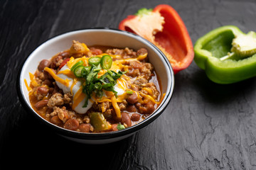 Texmex dish called "Chili con carne" with cheese and sour cream on dark background