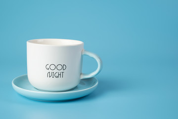 A white Cup on a saucer with an inscription on a blue background. Conveys freshness, vivacity of spirit.