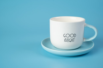 A white Cup on a saucer with an inscription on a blue background. Conveys freshness, vivacity of spirit.